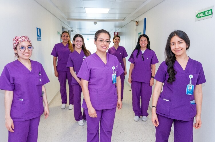 En un pasillo de una clínica se ven seis mujeres profesionales de la salud sonriendo. 